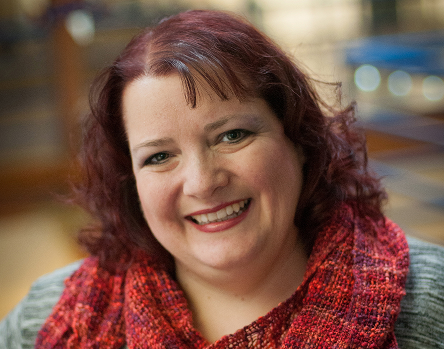 A photo of a woman smiling and wearing a red scarf.