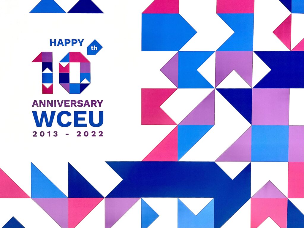 A banner reading "Happy 10th Anniversary WCEU" against a geometric blue, pink, and purple background.