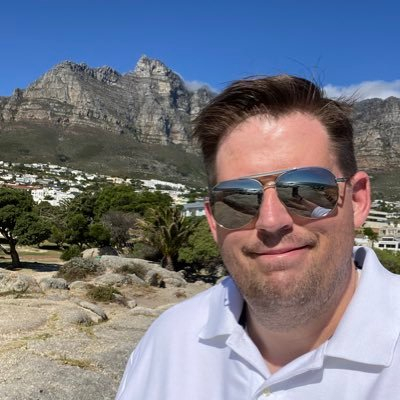 A photo of Ryan Don Sullivan wearing sunglasses with mountains in the background.