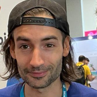 A photo of Aurelio smiling at the camera with a backwards hat and a lanyard on.