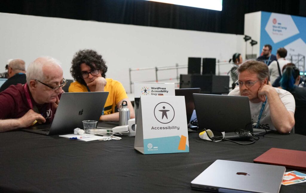 Three people are focused on laptops at a table with an "Accessibility" sign.