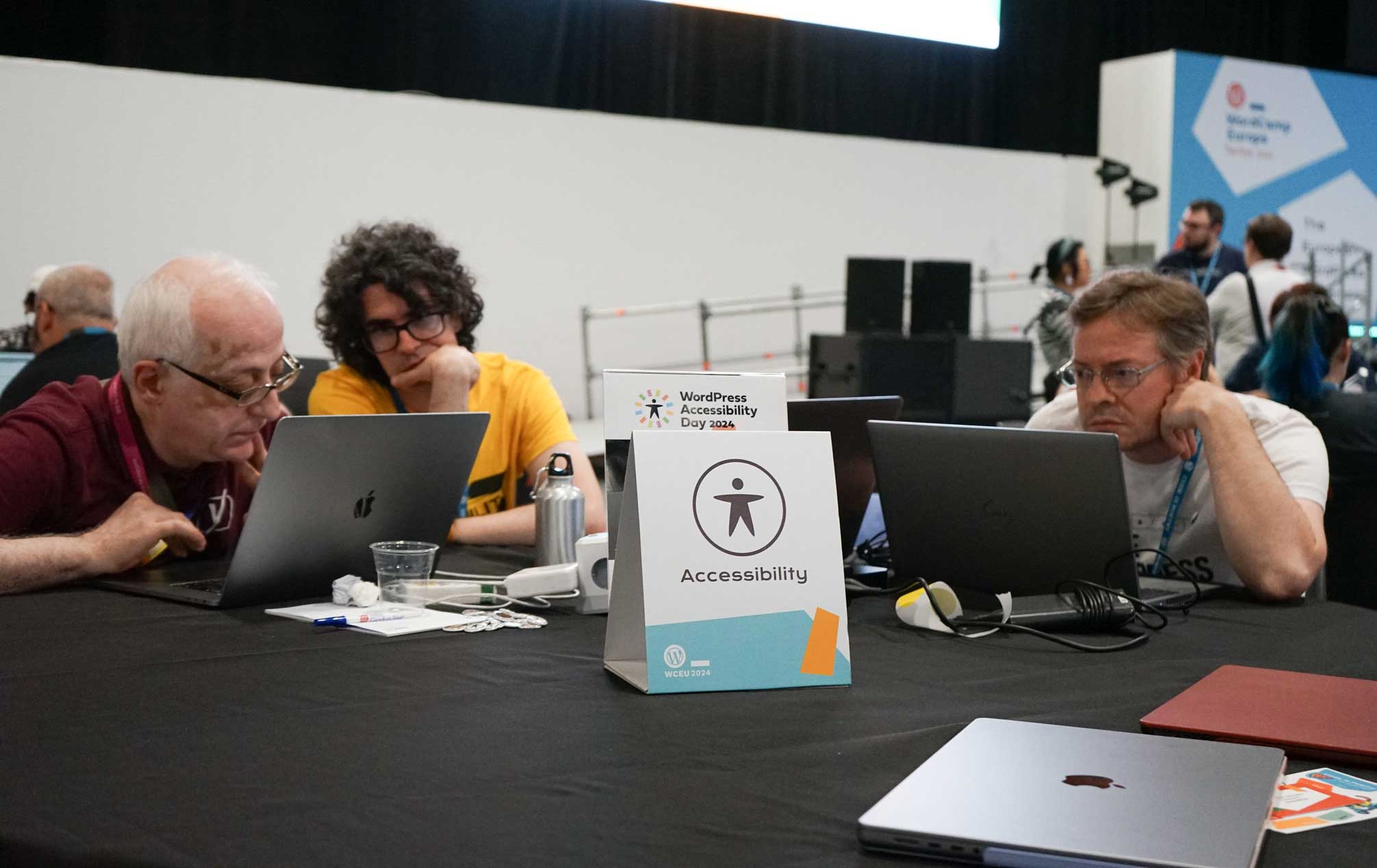 Three people are focused on laptops at a table with an "Accessibility" sign.