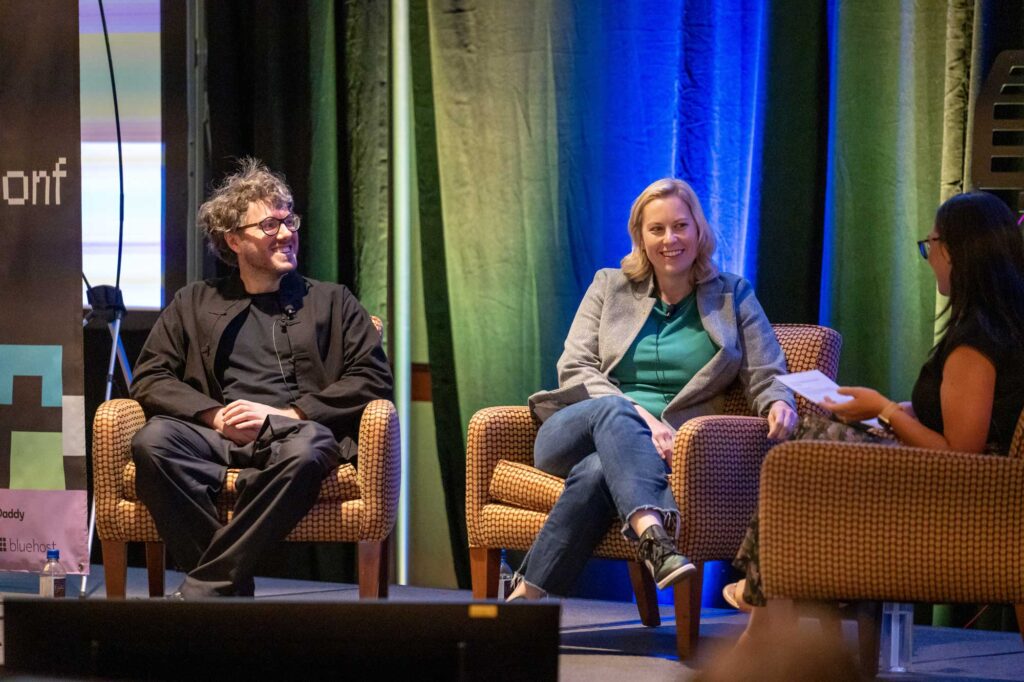 Two speakers sit on stage in armchairs, engaged in conversation during an event.