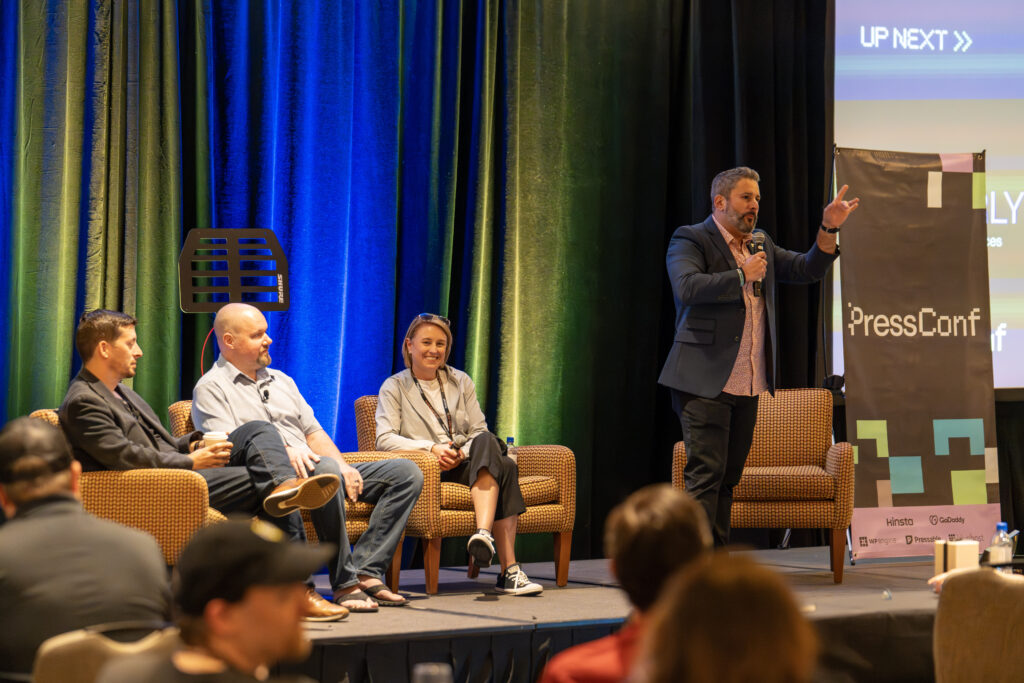 A panel discussion at a conference with four speakers on stage and a colorful backdrop.