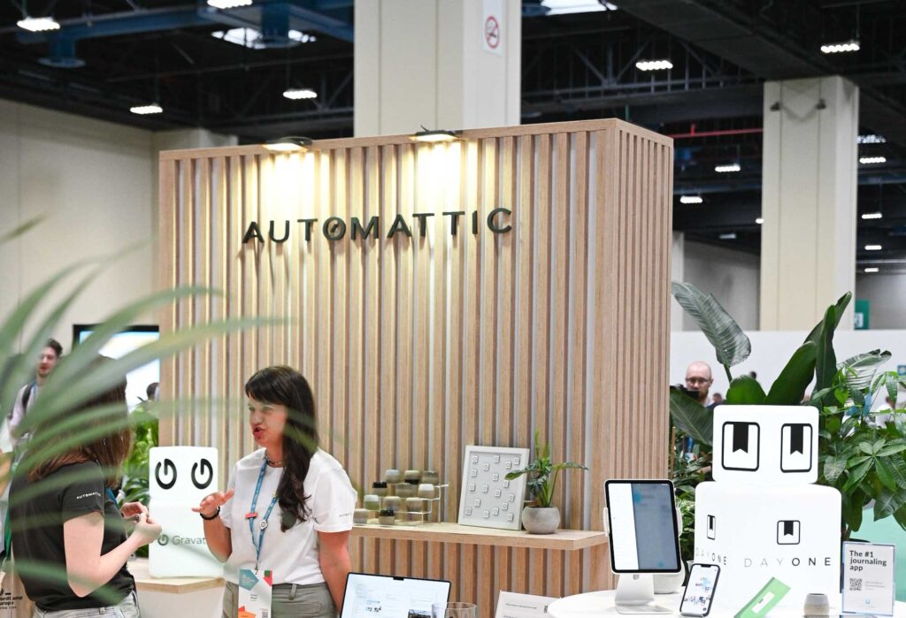 A booth with the name "AUTOMATTIC" featuring two women talking and plants around.