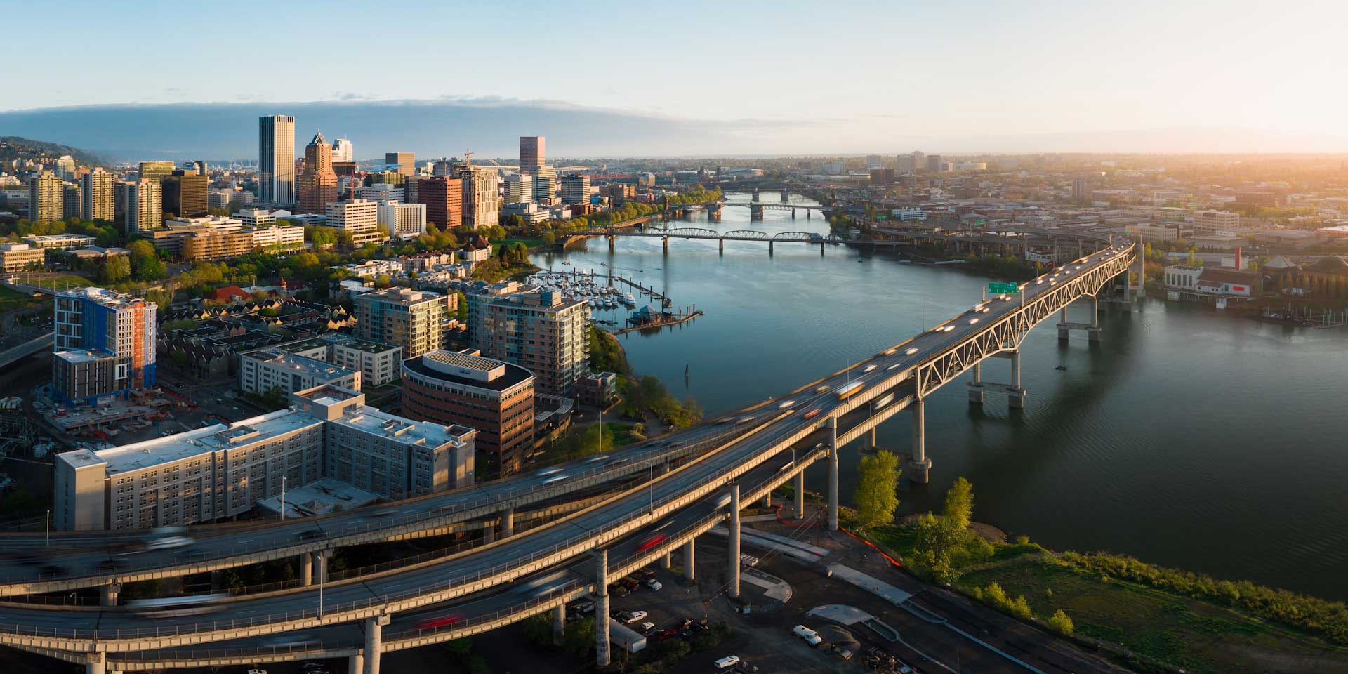 Aerial view of a city skyline with a river and bridges at sunset.