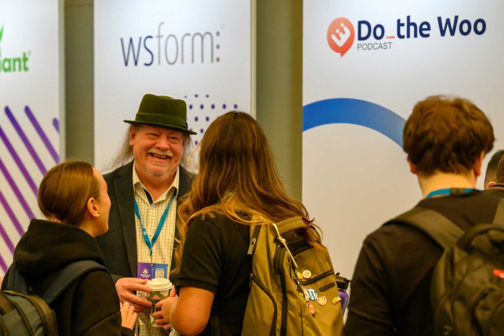A group of people chatting at a conference booth, with banners in the background.