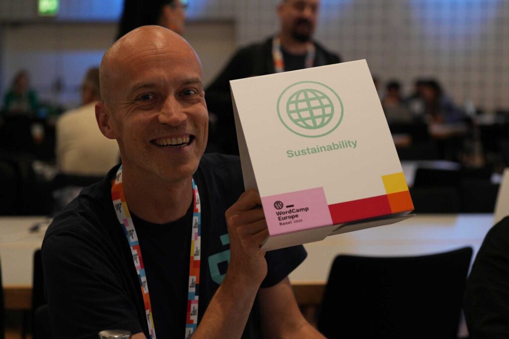 A smiling person holds a box labeled "Sustainability" at a conference.