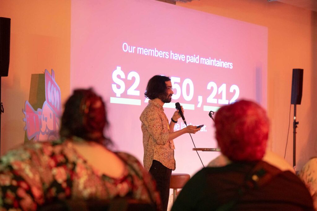 A speaker presents on stage with a slide showing "$2,250,212" to an audience.