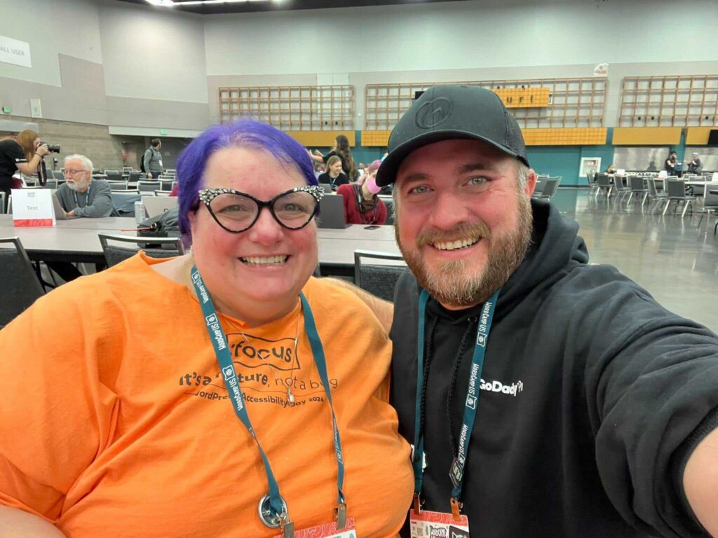Two smiling individuals take a selfie in a large conference space.